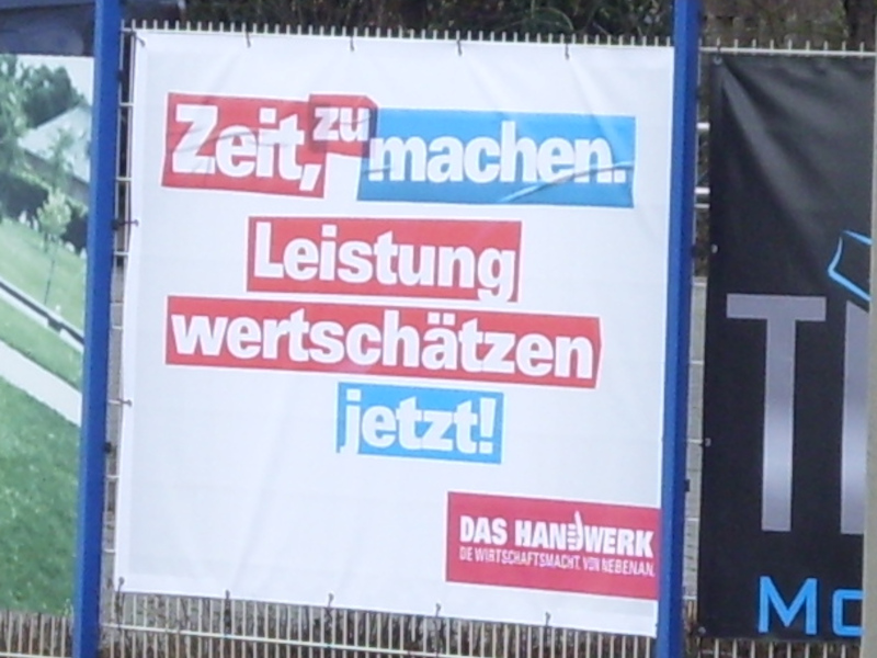 An einem Zaun hängendes Plakat mit folgendem Text: „Zeit, zu machen. Leistung wertschätzen jetzt! DAS HANDWERK. DIE WIRTSCHAFTSMACHT VON NEBENAN“