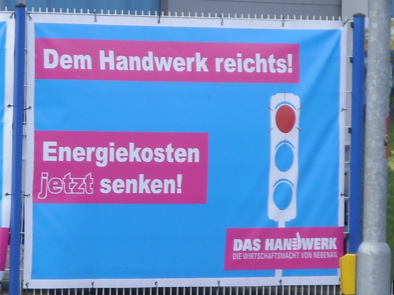An einem Zaun hängendes Plakat mit Ampel in den Farben Rot-Blau-Blau und folgendem Text: „Dem Handwerk reichts! Energiekosten jetzt senken! DAS HANDWERK, DIE WIRTSCHAFTSMACHT VON NEBENAN“